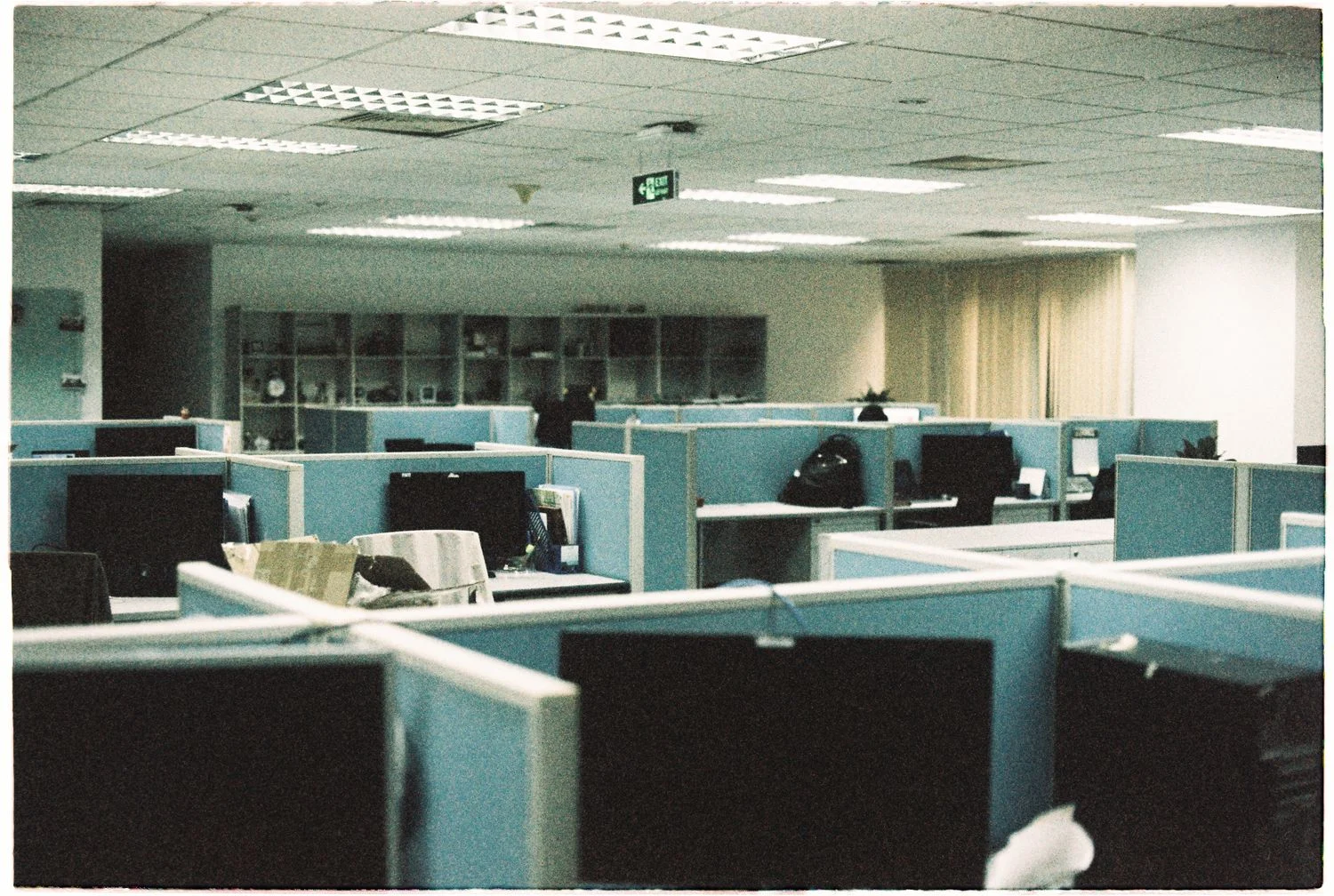 Rows of office cubicles with computer monitors and fluorescent lights.
