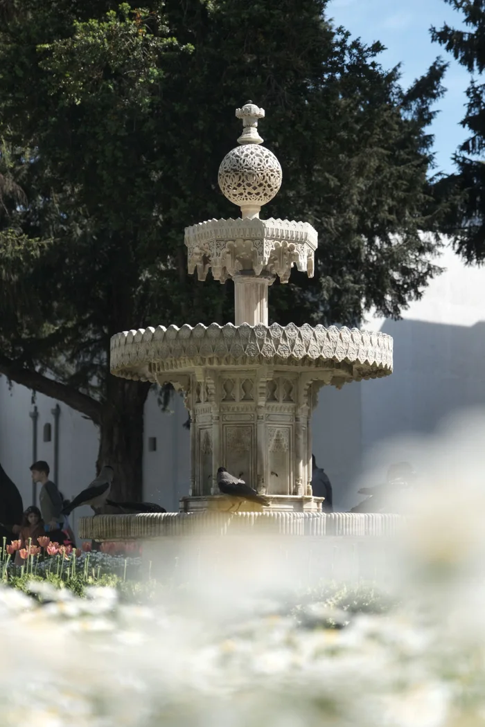 Beautiful ornate stone fountain surrounded by flowers in a sunny garden in Turkey.