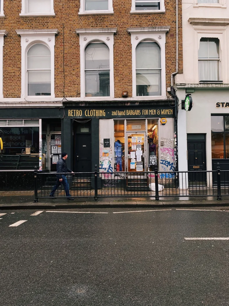 Exterior of a retro clothing shop on a rainy London street, showcasing urban life and fashion.