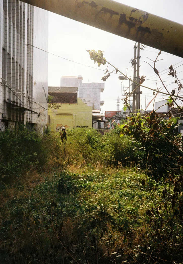An abandoned, overgrown urban area in Malang, Indonesia, with buildings and plants.