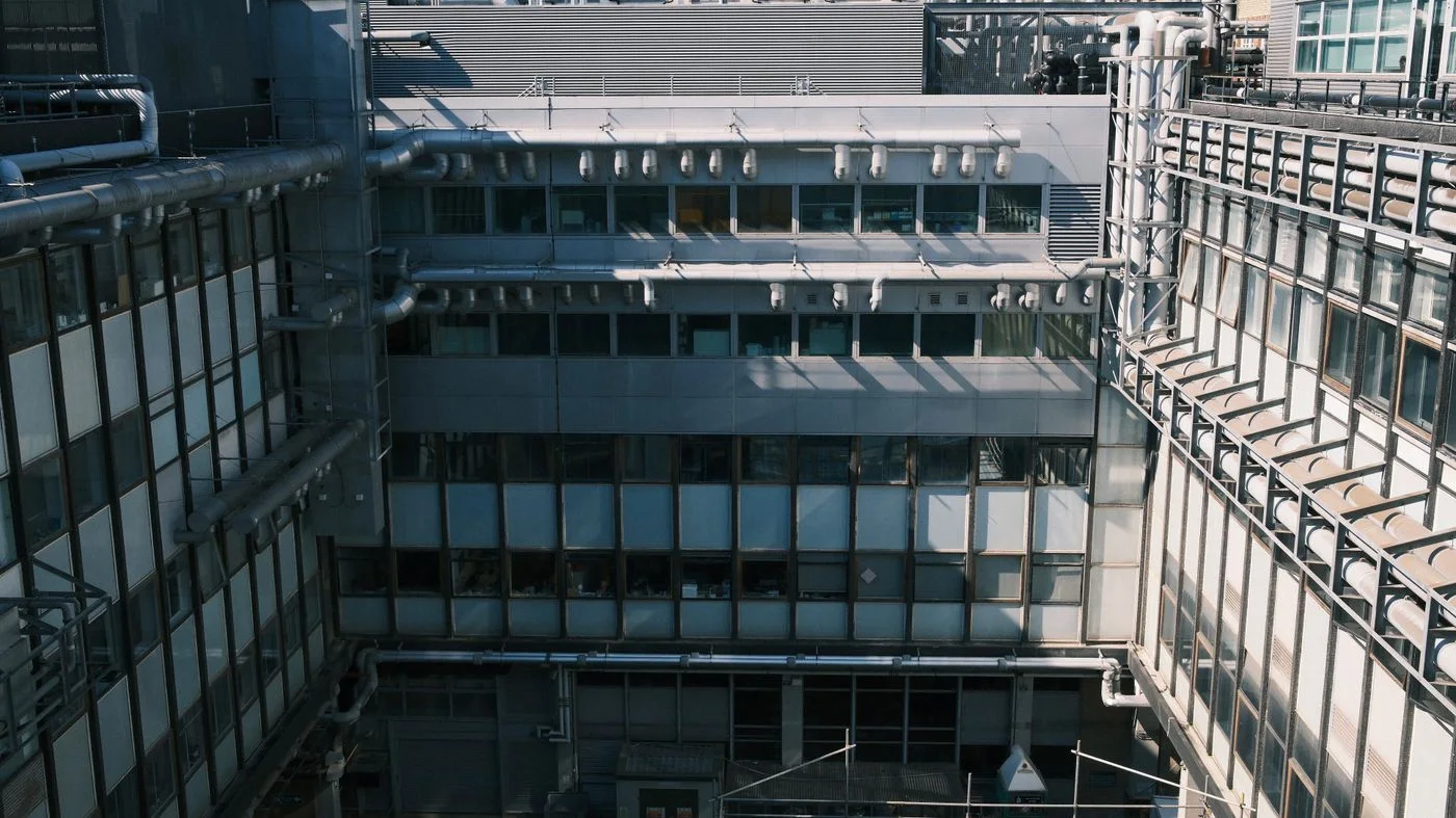 Photo of an industrial style building facade with exposed pipes and large windows, captured during the day.