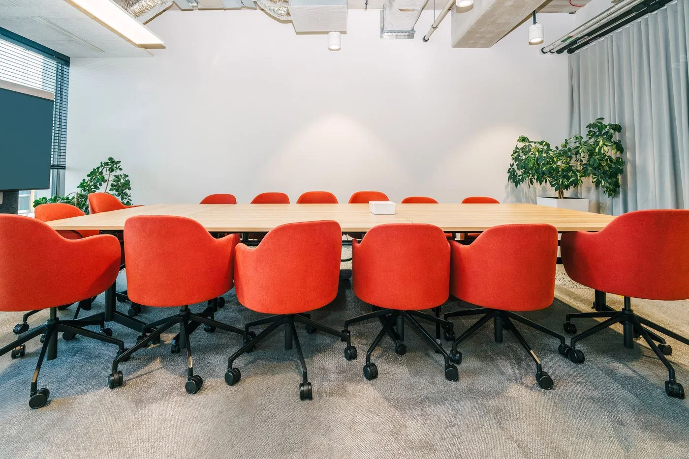 Interior of an empty boardroom featuring red chairs and a wooden table, perfect for corporate meetings.