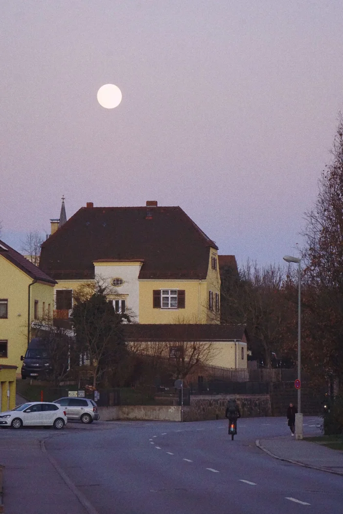 Quaint street scene during twilight in a small town with a visible full moon.