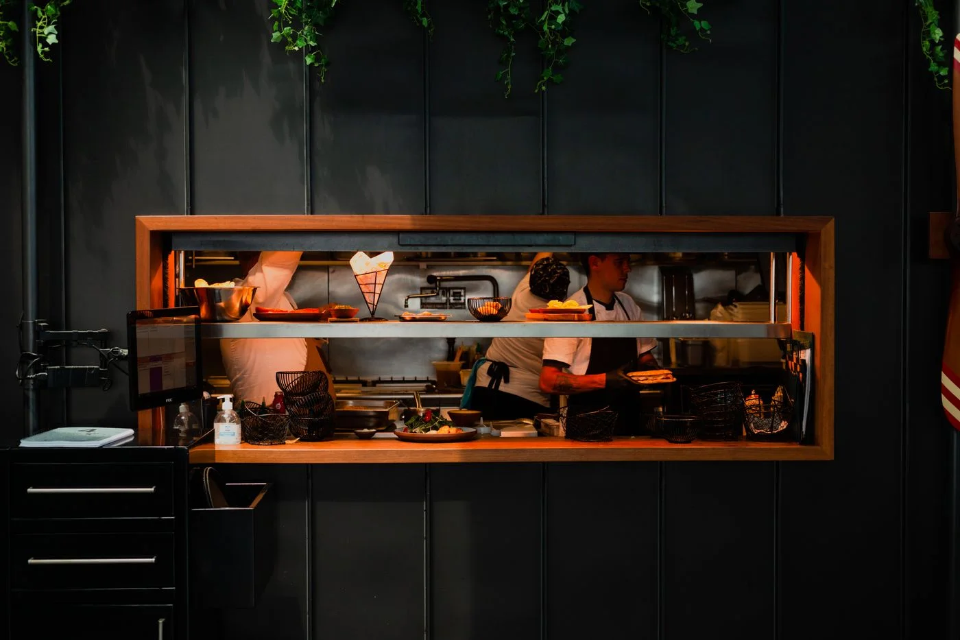 Chefs working in a lively restaurant kitchen through a serving pass.