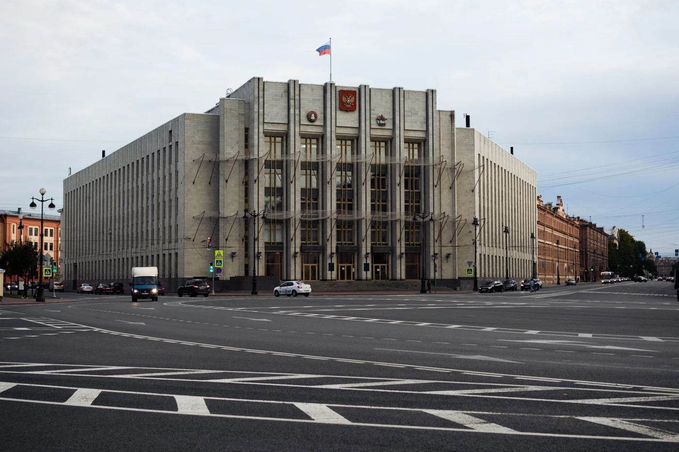A large government building with a flag at a major urban intersection on an overcast day.