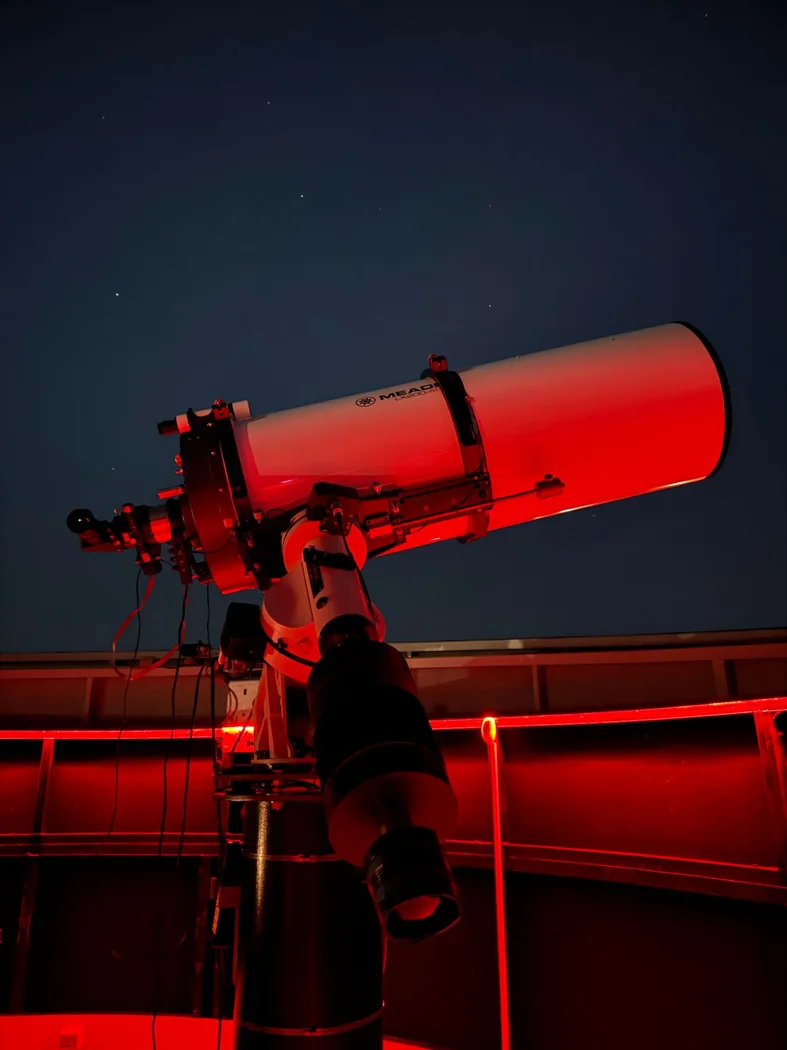 A telescope inside a red-lit observatory pointed at the night sky, capturing celestial views.