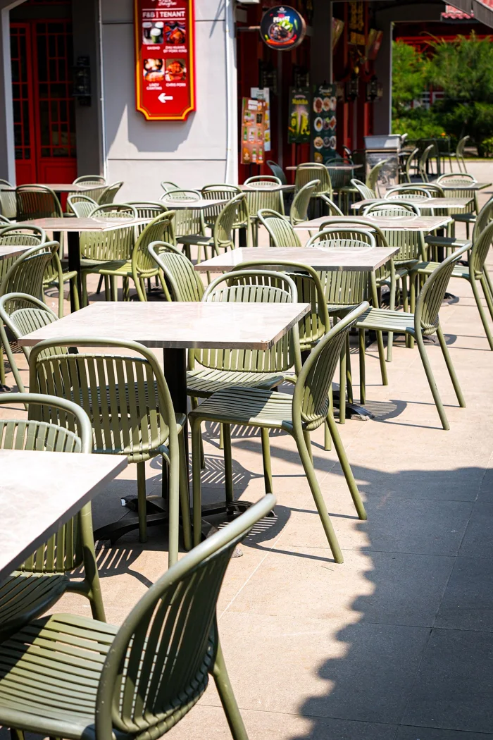 Sunlit empty tables and chairs at a modern outdoor cafe patio, inviting atmosphere.