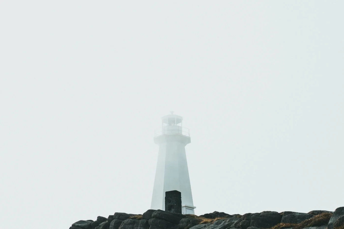 Misty view of a lighthouse emerging from the fog on a rocky coastline, symbolizing guidance and safety.
