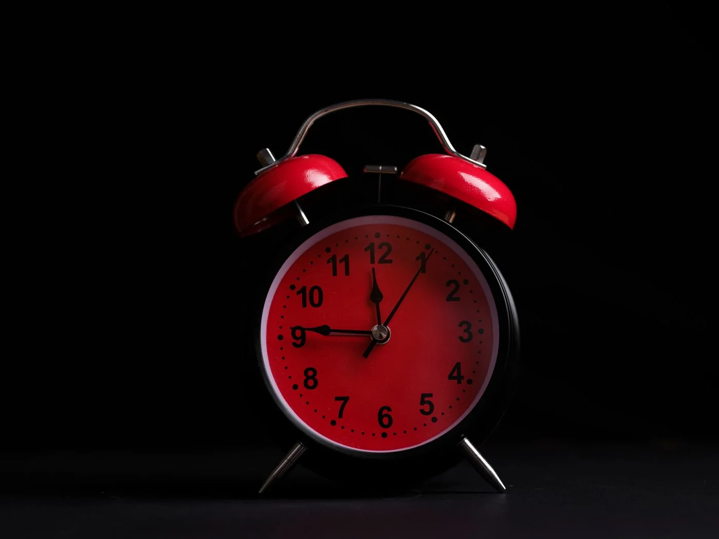 A red analog alarm clock against a dark background.