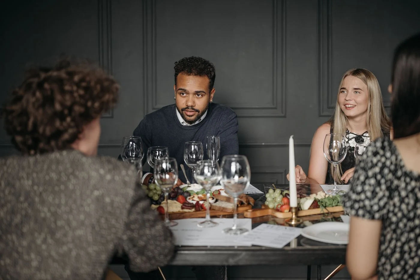 Group of friends having a conversation at a dining table set with food and drinks indoors.