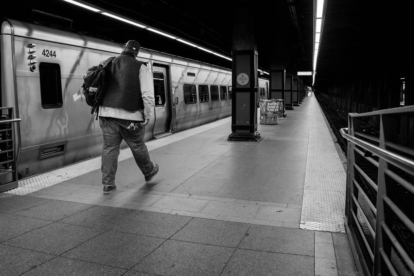 Black and white image of a lone traveler walking on a New York subway platform beside a train.