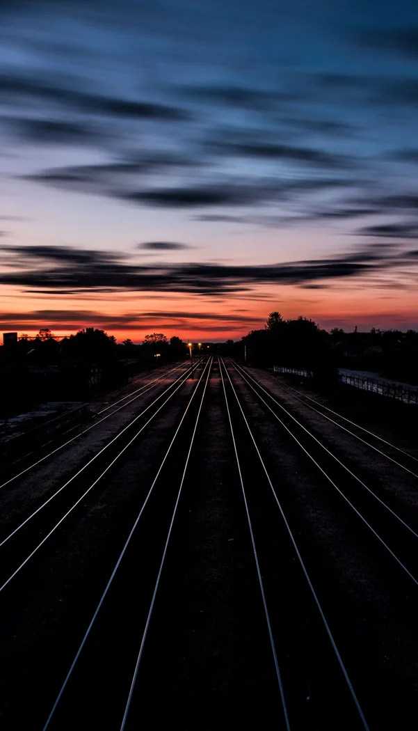Long railway tracks stretching into the horizon under a dramatic twilight sky.
