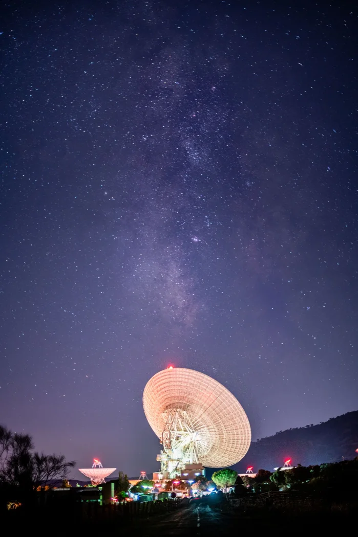 Satellite dishes under a vibrant starry night sky, highlighting the Milky Way.