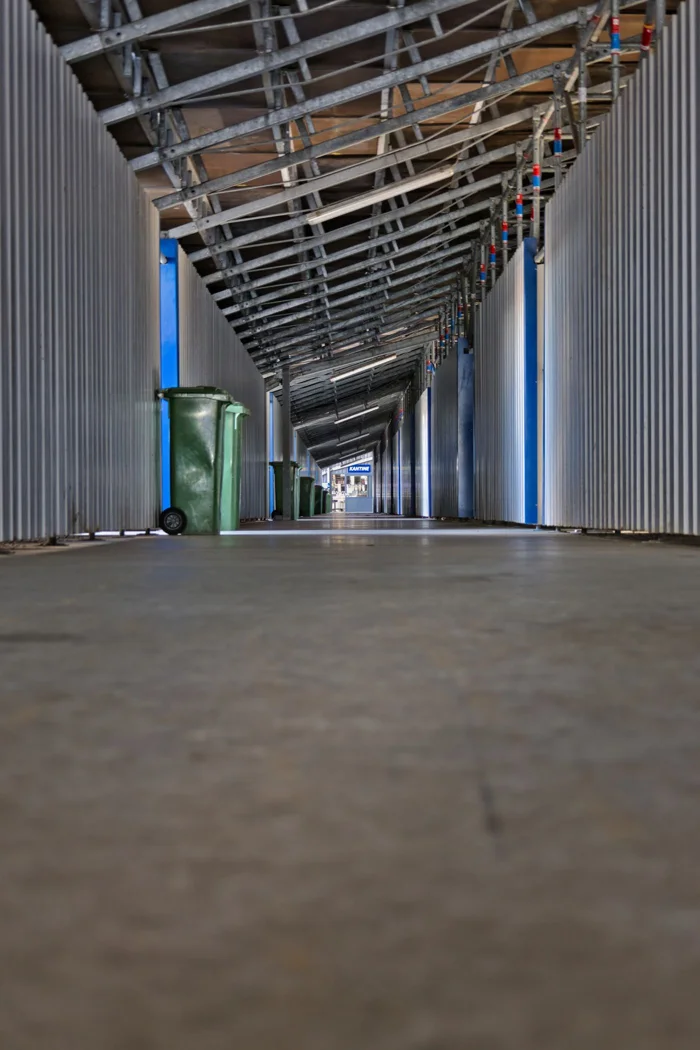 Long industrial corridor with metal beams and waste bins, featuring modern design.