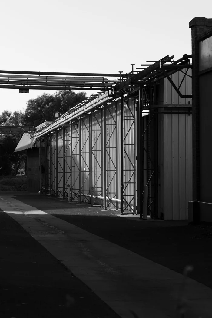 Black and white photograph of an industrial warehouse with metal framework outdoors.