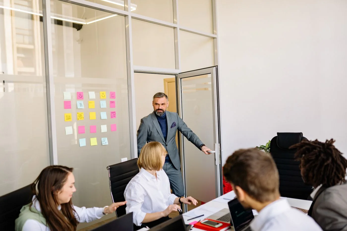 Business team collaborating in a conference room with post-it notes on a glass door.
