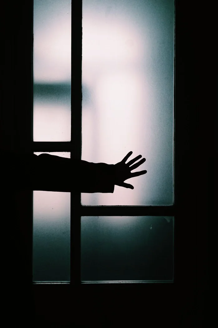 Silhouette of a hand touching a frosted glass door, creating a mysterious atmosphere.