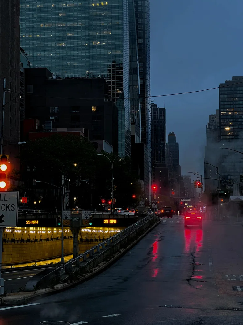 Moody city street in New York with wet roads and city lights during a rainy evening.