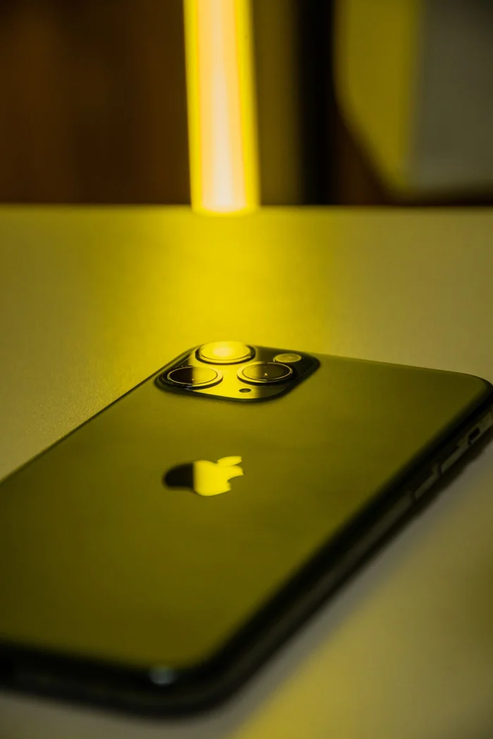 A modern smartphone placed on a table under ambient yellow lighting, showcasing sleek design.