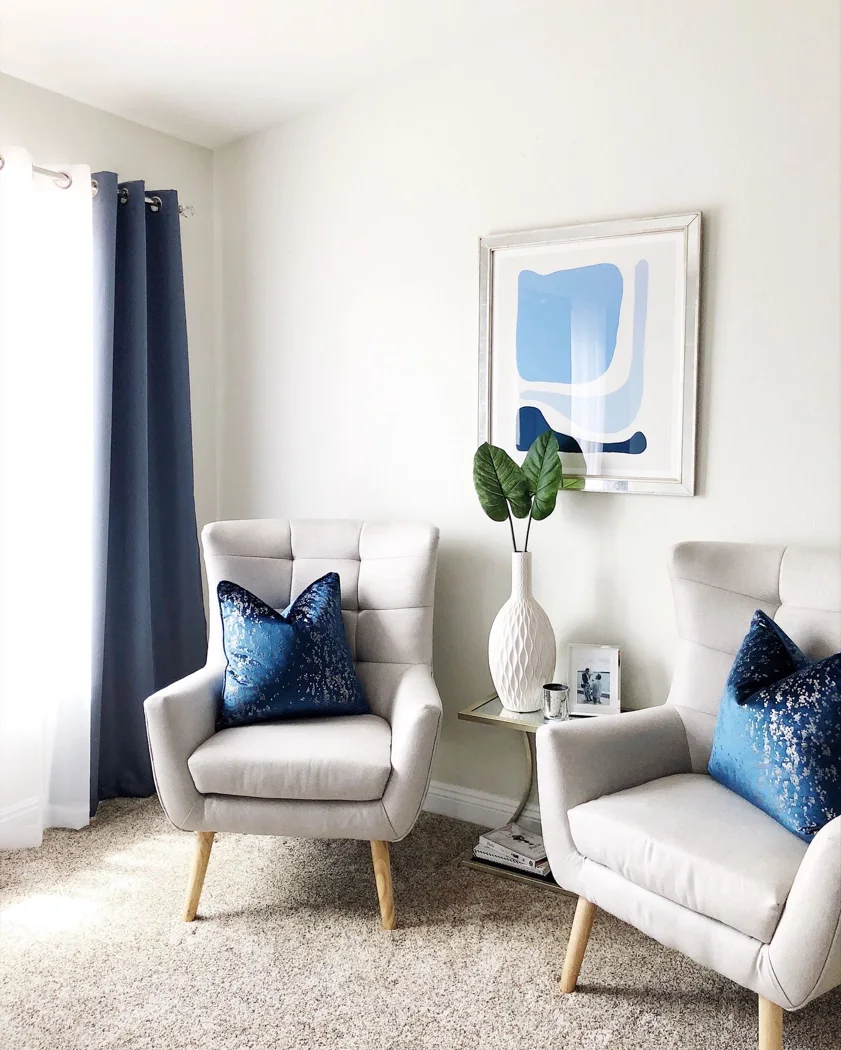 Modern living room with two chairs, blue pillows, and abstract art.